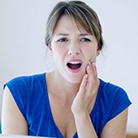 Woman in blue shirt rubbing her jaw due to discomfort