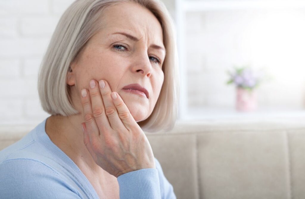 An older woman holding her jaw in pain.